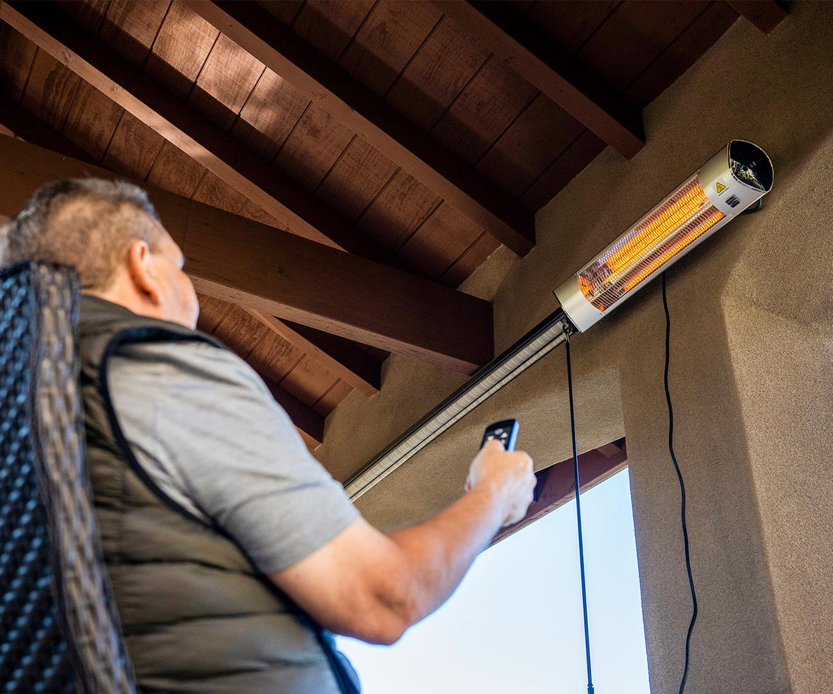Man on a covered patio pointing the remote at the wall-mounted Kenmore heater above him